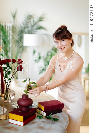 Close up of bouquet arrangement. Woman puts roses in vase on table at home. Fresh red blooms. Interior and decor 110472137