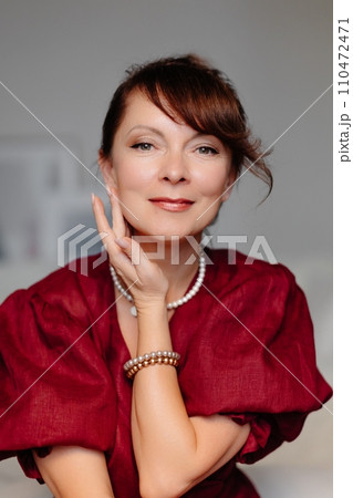 Adult woman in red dress sitting on couch in living room with classic design, having beautiful hairstyle 110472471