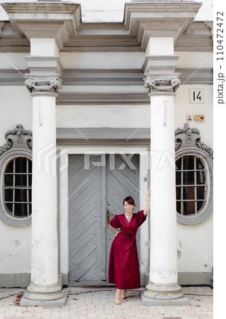 Attractive girl with hairstyle, in red dress is walking on street on old building background 110472472