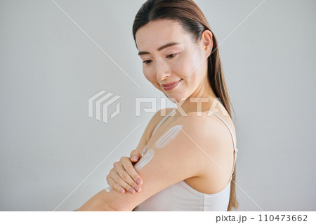 二の腕にクリームを塗ってボディケアする30代女性 110473662