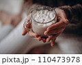 Transparent glass mug of cocoa with marshmallows in female hands. Close-up. New Year's portrait. 110473978