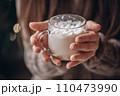 Transparent glass mug of cocoa with marshmallows in female hands. Close-up. New Year's portrait. 110473990