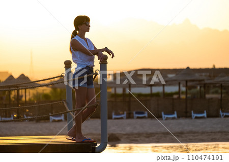 Young female tourist in casual clothes enjoying warm sunny evening on sea shore. Summer vacations and travelling concept. 110474191