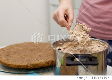 Working process of baking cake at home. Close up of female hand topping cream on chocolate biscuit. Culinary and delicious dessert concept. Working process of baking cake at home. Close up of female hand topping cream on chocolate biscuit. Culinary and delicious dessert concept. 110474197