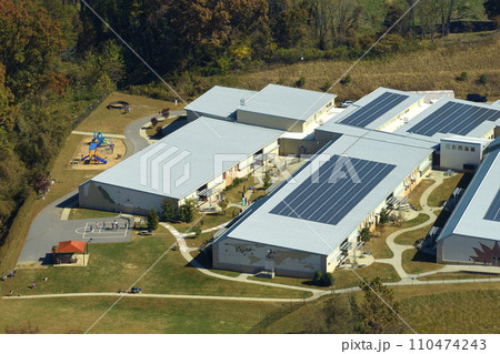 View from above of american school campus with roof covered with photovoltaic solar panels for producing of electrical clean energy View from above of american school campus with roof covered with photovoltaic solar panels for producing of electrical clean energy 110474243
