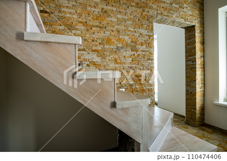 Stylish wooden contemporary staircase inside loft house interior. Modern hallway with decorative limestone brick walls and white oak stairs. 110474406