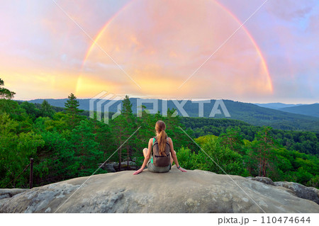 Hiker woman resting on rocky mountain top enjoying morning nature during her travel on wilderness trail. Lonely female traveler traversing high hilltop route. 110474644