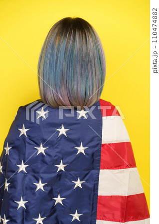 Patriotic Pride And Freedom Spirit Of United States And Its Cultural Richness. Girl With Multicolored Hair Covered With American Flag, Isolated On Yellow Backdrop, Backside View. High quality photo 110474882
