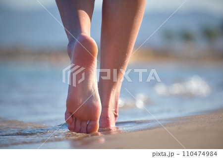Close up of female feet walking barefoot on white grainy sand of golden beach on blue ocean water background 110474984