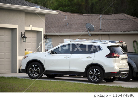 Car parked in front of wide garage double door on concrete driveway of new modern American house Car parked in front of wide garage double door on concrete driveway of new modern American house 110474996