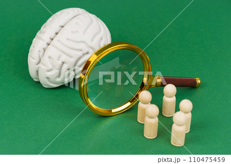 On a white background, a model of the brain, a magnifying glass and wooden human figures. 110475459