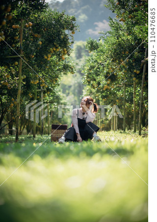 A happy woman farmer is resting in orchard or orange farm. A happy woman farmer is resting in orchard or orange farm. 110476685