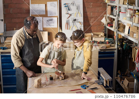 High angle view at children painting wooden toy model in carpenting workshop, Black teacher watching 110476786