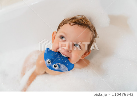 Close-up portrait of cute little boy playing with toy in bathtub with foam Close-up portrait of cute little boy playing with toy in bathtub with foam 110476942