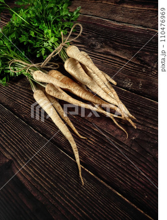 Bunch of parsnips with green leaves on dark wooden desk. 110476969