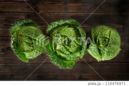 Three savoy cale cabbage heads on dark wooden board, view from above Three savoy cale cabbage heads on dark wooden board, view from above 110476971