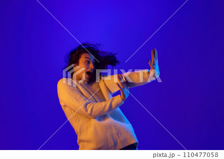 Stop negative. Dynamic portrait of young woman put her hands forward as stop sign and falls in motion against blue gradient background. Stop negative. Dynamic portrait of young woman put her hands forward as stop sign and falls in motion against blue gradient background. 110477058