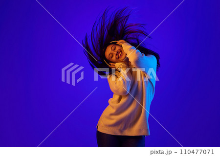 Elevated Energy. Dynamic portrait of girl in headphones energetically shakes her head to rhythm of music and her hair develops in movement. 110477071