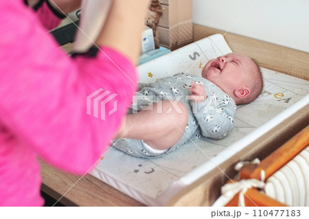 4 months old baby infant boy on changing board, crying as mother is putting his clothes on 110477183