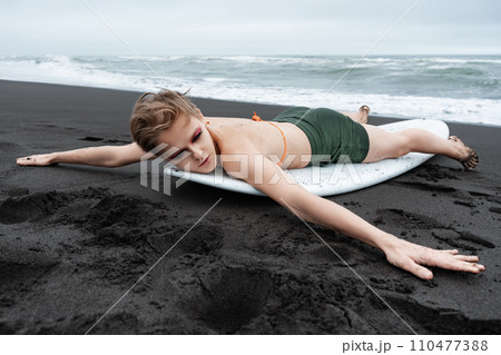 Female surfer is lying on surfboard on beach with arms outstretched to sides after surfing training 110477388