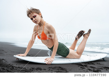 Sports fashion model surfer lying on surfboard, leaning on hands, arching back and looking at camera 110477390