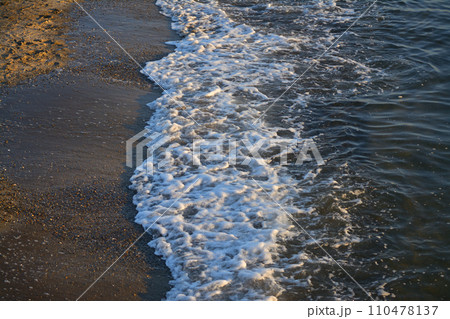 夕暮れ時の浜辺に寄せる波 110478137