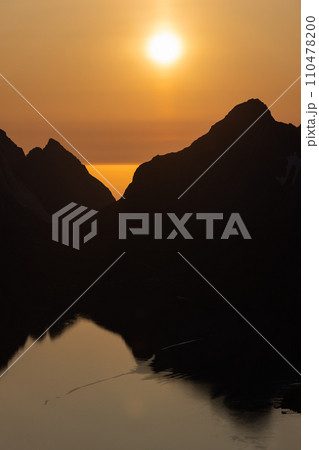 Golden midnight sun silhouettes Reinebringen, mirrored in Lofoten's calm waters 110478200