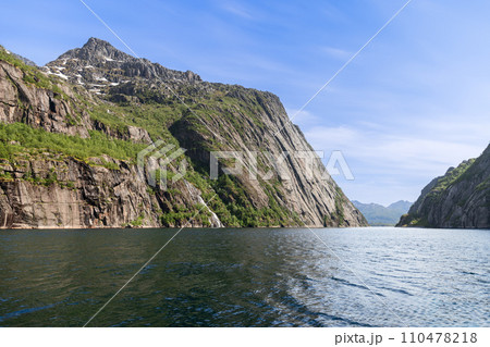 Snow-dotted cliffs tower over Trollfjorden's serene waters in the Lofoten Islands 110478218