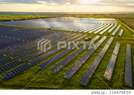Aerial view of large sustainable electrical power plant with many rows of solar photovoltaic panels for clean ecological electric energy at sunrise. Renewable electricity with zero emission concept. Aerial view of large sustainable electrical power plant with many rows of solar photovoltaic panels for clean ecological electric energy at sunrise. Renewable electricity with zero emission concept. 110478634