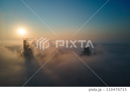 Aerial view of cement factory with high concrete plant structure and tower crane at industrial production site on foggy morning. Manufacture and global industry concept. Aerial view of cement factory with high concrete plant structure and tower crane at industrial production site on foggy morning. Manufacture and global industry concept. 110478715