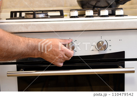 A hand turns the knob on the oven panel. A hand turns the knob on the oven panel. 110479542