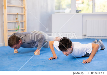Father and son train abdominal muscles in gym - perform plank exercise Father and son train abdominal muscles in gym - perform plank exercise 110480144