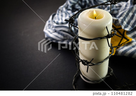 Holocaust memory day. Arbed wire and burning candle on black background Holocaust memory day. Arbed wire and burning candle on black background 110481282