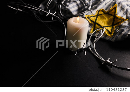 Holocaust memory day. Arbed wire and burning candle on black background Holocaust memory day. Arbed wire and burning candle on black background 110481287