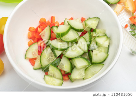 Bowl with pieces of sweet pepper and cucumber for preparing salad. Bowl with pieces of sweet pepper and cucumber for preparing salad. 110481650