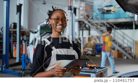 Certified repairman in auto repair shop showing customer what needs to be changed on her car for it to properly work. Garage expert inspecting vehicle placed on overhead lift, talking with woman Certified repairman in auto repair shop showing customer what needs to be changed on her car for it to properly work. Garage expert inspecting vehicle placed on overhead lift, talking with woman 110481757