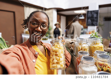 POV of a black woman wearing glasses, holding a glass container filled with pasta in a bio-food supermarket. Online marketing, organic items, vlogging, digital camera, customer filming. POV of a black woman wearing glasses, holding a glass container filled with pasta in a bio-food supermarket. Online marketing, organic items, vlogging, digital camera, customer filming. 110481784