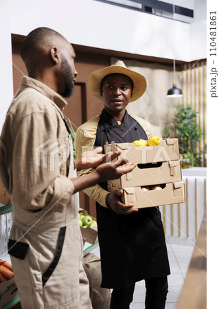 Local farmer supplies organic items to satisfied vendor who serves sustainability-minded clients in a zero-waste store. Young guy gives crates full of freshly harvested, wholesome produce to retailer. Local farmer supplies organic items to satisfied vendor who serves sustainability-minded clients in a zero-waste store. Young guy gives crates full of freshly harvested, wholesome produce to retailer. 110481861