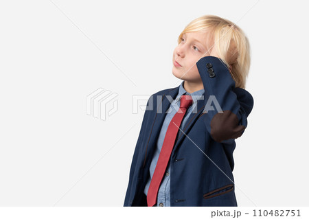 Thoughtful boy with blond hair dressed in blue shirt, red tie and blue jacket standing with hand on chin and looking away isolated over white background Thoughtful boy with blond hair dressed in blue shirt, red tie and blue jacket standing with hand on chin and looking away isolated over white background 110482751