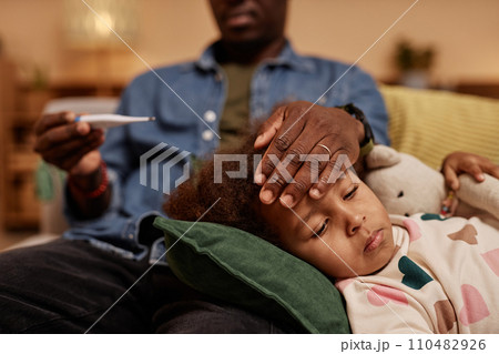 Close up shot of sick African American preschool girl lying on dads knee while he measuring her temperature Close up shot of sick African American preschool girl lying on dads knee while he measuring her temperature 110482926