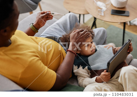 High angle view of sick African American girl using tablet with caring father checking her temperature 110483031