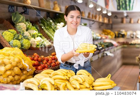 Cheerful young female shopper selecting ripe bananas in store 110483074