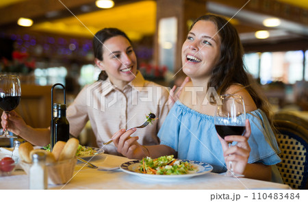 Two girls are discussing something fun at a table in restaurant 110483484