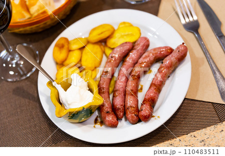 Fried butifarra sausages with fried potato slices are served on plate 110483511