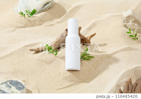 Against the sand background with gray and beige stones, dry twig and grass, a white cosmetic tube displayed. Mockup scene for advertising, summer beach concept 110485420