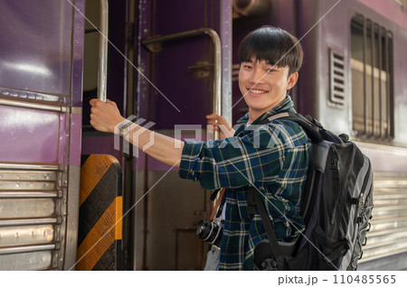 A happy Asian man backpacker is getting on the train, travel somewhere on his summer vacation. A happy Asian man backpacker is getting on the train, travel somewhere on his summer vacation. 110485565