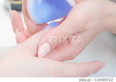 ネイルサロン_ハンディライト（LED）でジェルを固めている 110485722