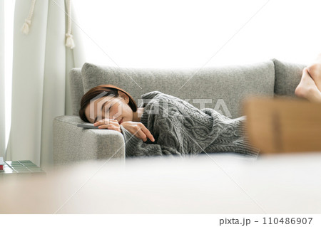 ソファで寝転んでスマホを使う女性 110486907
