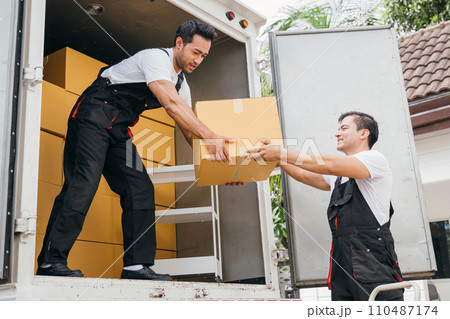 Smiling employees of a removal company work in uniform unloading boxes and furniture from the truck. Their dedication guarantees a smooth delivery into the new home ensuring happiness. Moving Day 110487174