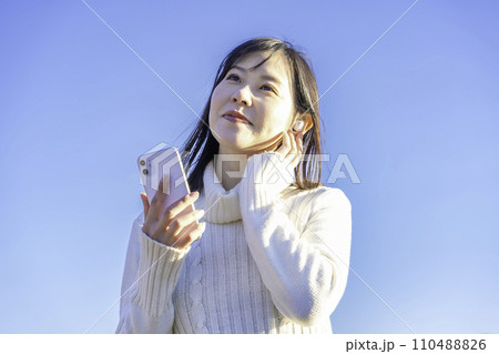 青空の下でスマホ音楽を聴く女性 110488826
